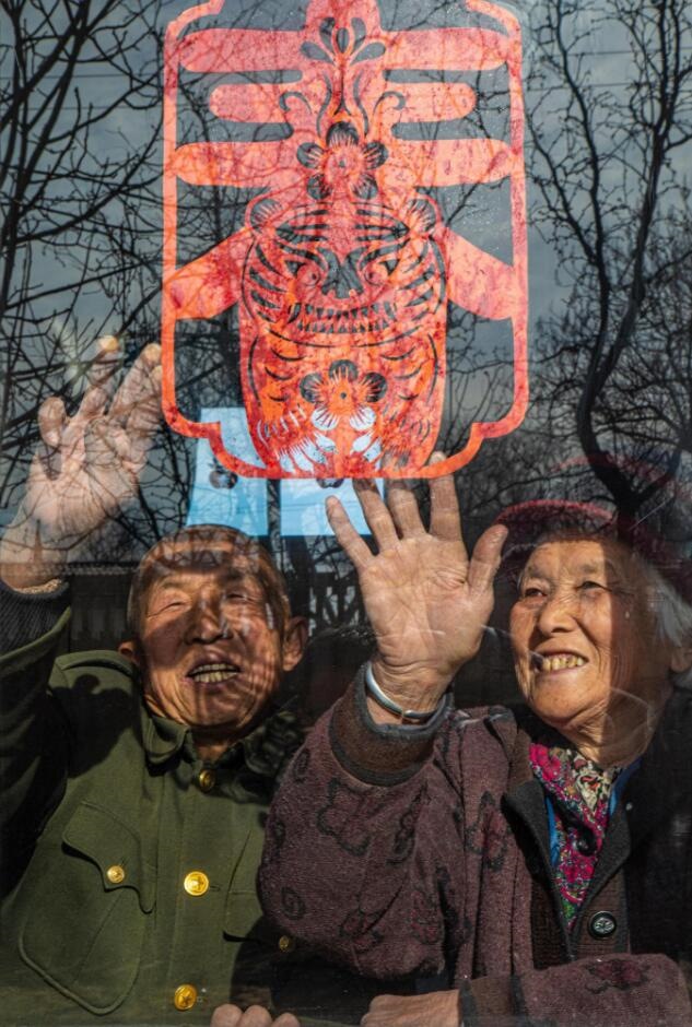 臘月里，霍州市師莊鄉(xiāng)馮南垣村村民師榮光(左)在災(zāi)后重建的新家里貼窗花。(霍州市委宣傳部供圖)