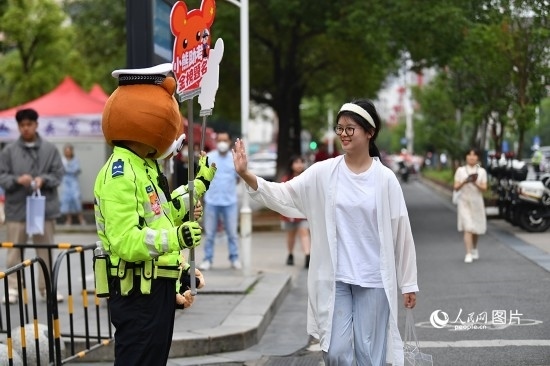 6月7日上午9時(shí)，隨著鈴聲的響起，2023年江西高考正式開(kāi)考，江西省的53.57萬(wàn)考生以縣（區(qū)）為單位隨機(jī)安排在全省256個(gè)考點(diǎn)、18968個(gè)考場(chǎng)參加高考。圖為“小熊交警”和考生擊掌鼓勵(lì)。 人民網(wǎng)記者 時(shí)雨攝